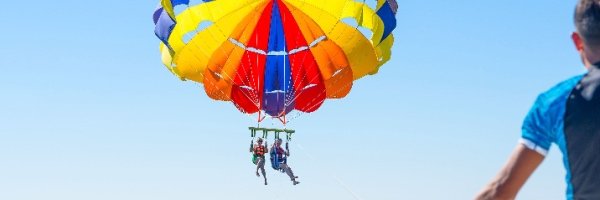 Happy couple Parasailing in Dubai beach in summer. Three people rest on the sea. Parachute and water skiing.