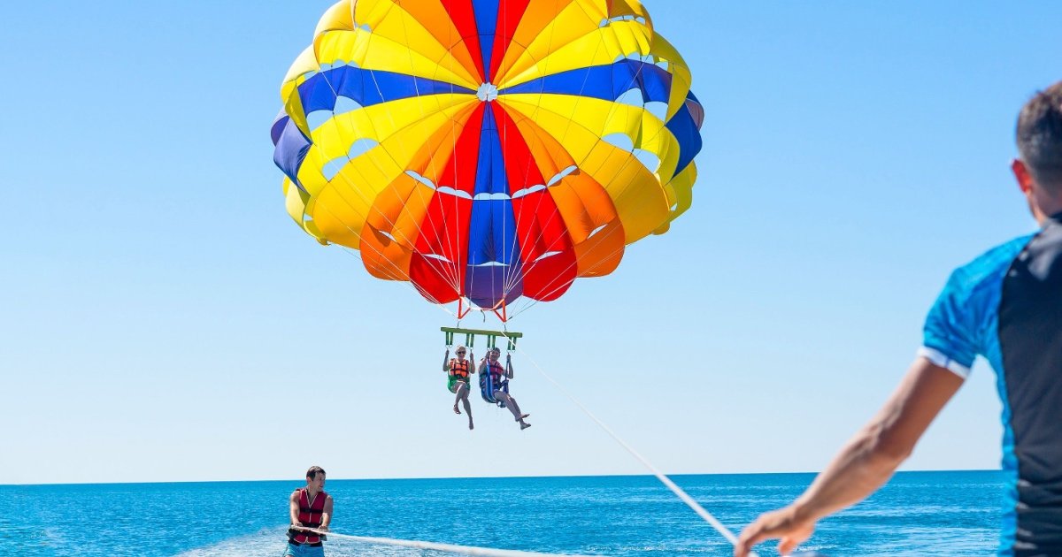 Happy couple Parasailing in Dubai beach in summer. Three people rest on the sea. Parachute and water skiing.
